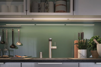 Moderne Küchenzeile mit Edelstahl-Spültischarmatur, grüner Glasrückwand und LED-Unterbauleuchte