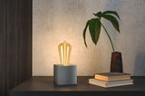 Moderne Tischleuchte mit warmweißem LED-Leuchtmittel auf grauem Würfel aus Metall für Wohnräume
