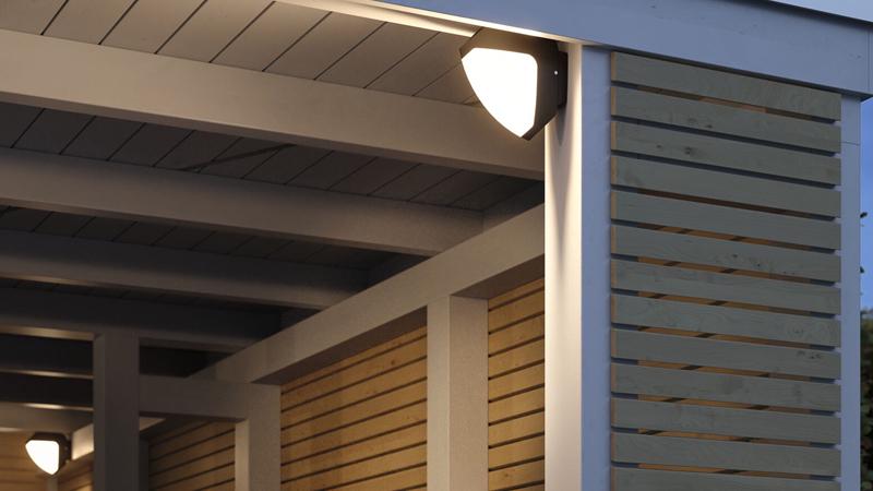 Witte kunststof buitenwandlamp op modern houten terras die de ingang verlicht, LED buitenverlichting.