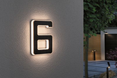 Numéro de maison 6 noir éclairé par LED blanc chaud sur mur extérieur.
