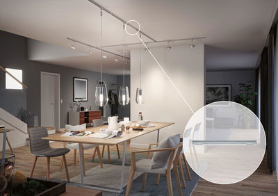 Moderne eetkamer met houten stoelen en glazen hanglampen, metalen railsysteem voor LED-verlichting in beeld