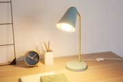 Moderne Schreibtischlampe mit mintgrünem Metallfuß und goldfarbenem Arm, beleuchtet Arbeitsfläche mit Uhr und Stiftehalter.