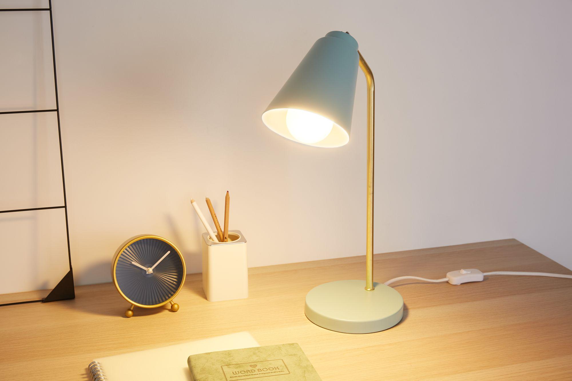 Moderne Schreibtischlampe mit mintgrünem Metallfuß und goldfarbenem Arm, beleuchtet Arbeitsfläche mit Uhr und Stiftehalter.
