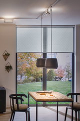 Modern dining area with wooden table, black chairs, and two gray pendant lamps in front of large windows with patterned blinds