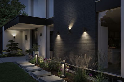 Moderne Außenbeleuchtung mit schwarzen Wandlampen und Bodeneinbauleuchten an Hausfassade und Gartenweg