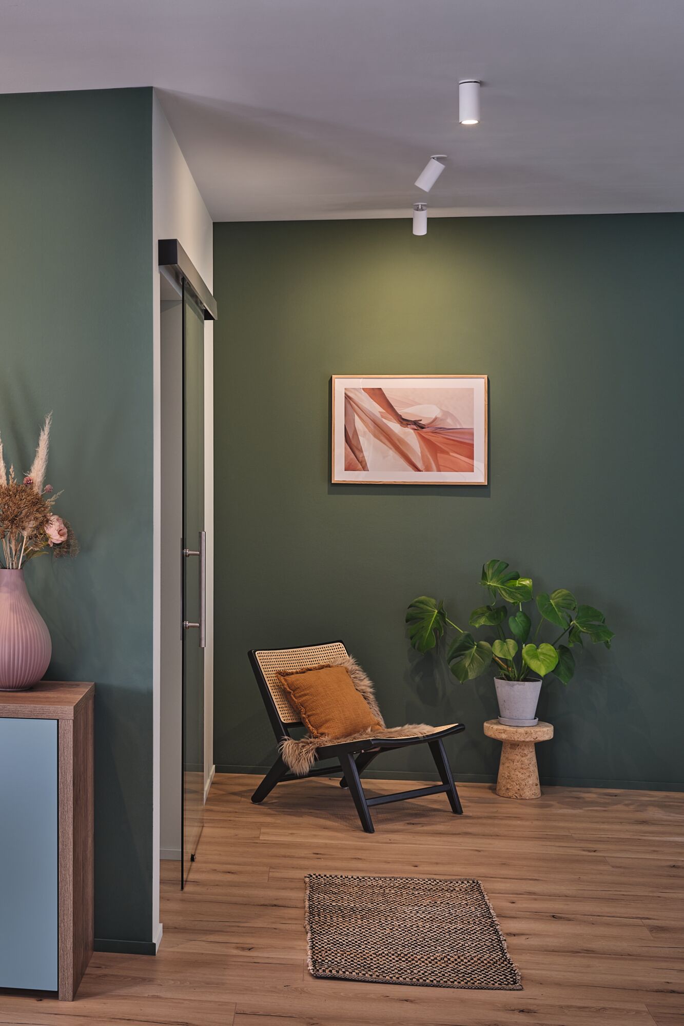 Salon moderne avec mur vert, chaise en bois, plante et spots LED de plafond Paulmann.