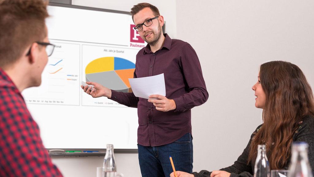 Mann präsentiert Diagramme bei Meeting, Tipps für Karriere und Bewerbung im Bürokontext.