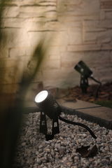 Black metal outdoor LED spotlight on gravel with warm white light for garden lighting