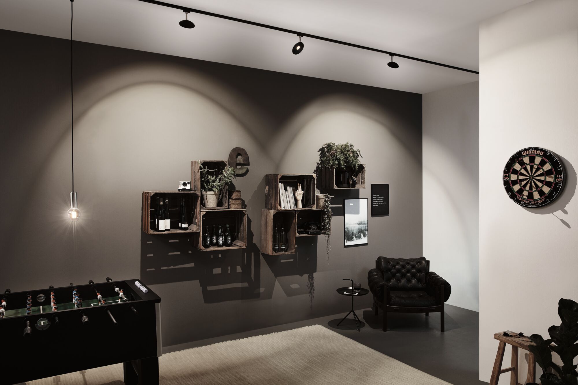 Modern living room with black leather armchair, wooden crate shelves, dartboard and foosball table under LED spotlights