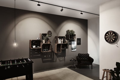 Modernes Wohnzimmer mit schwarzem Ledersessel, Holzkistenregal, Dartboard und Foosball-Tisch unter LED-Spots