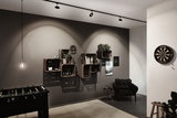 Modernes Wohnzimmer mit schwarzem Ledersessel, Holzkistenregal, Dartboard und Foosball-Tisch unter LED-Spots