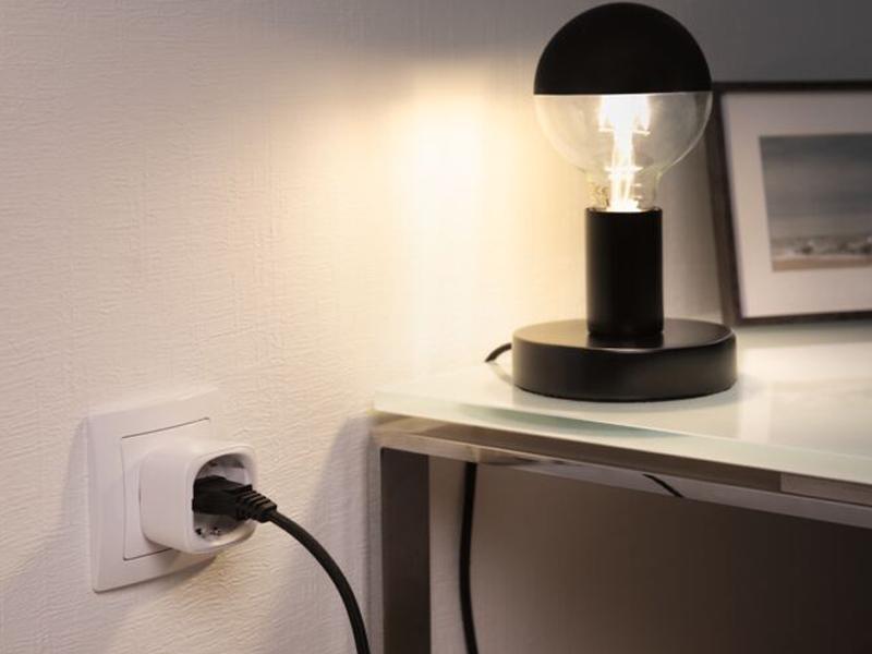Zwarte tafellamp met glazen bol en slimme stekkeradapter aan witte muur in moderne kamer