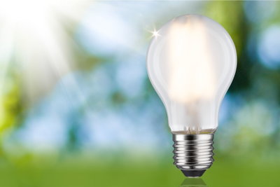 Glowing LED light bulb with clear glass and metal base against green-blue blurred background