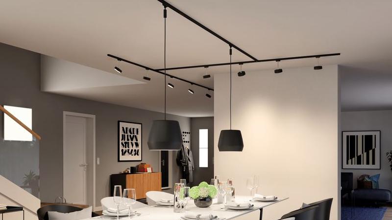 Salle à manger moderne avec système de rails noir et suspensions au-dessus d'une table blanche dressée.