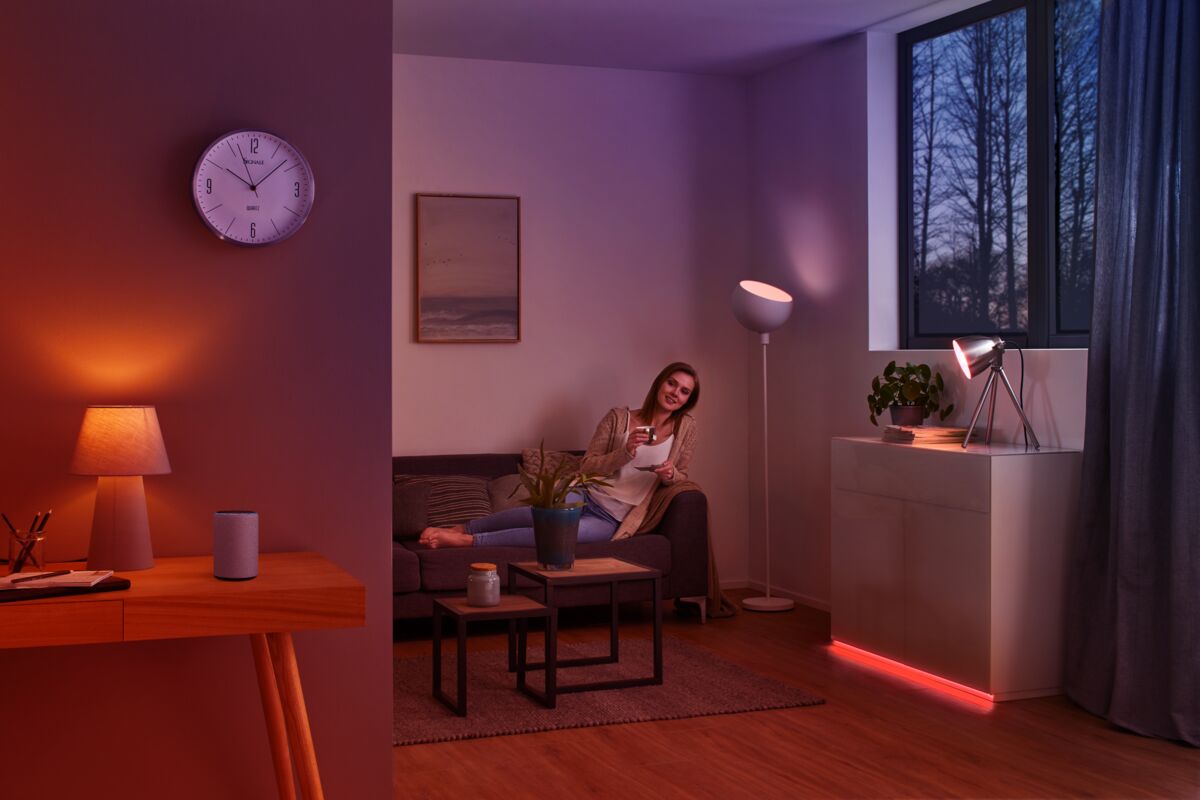 Salon avec éclairage moderne en tons chauds et violets, femme détendue sur canapé avec télécommande