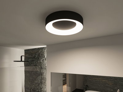 Plafonnier rond noir avec anneau LED blanc chaud dans salle de bain moderne avec mur en pierre.