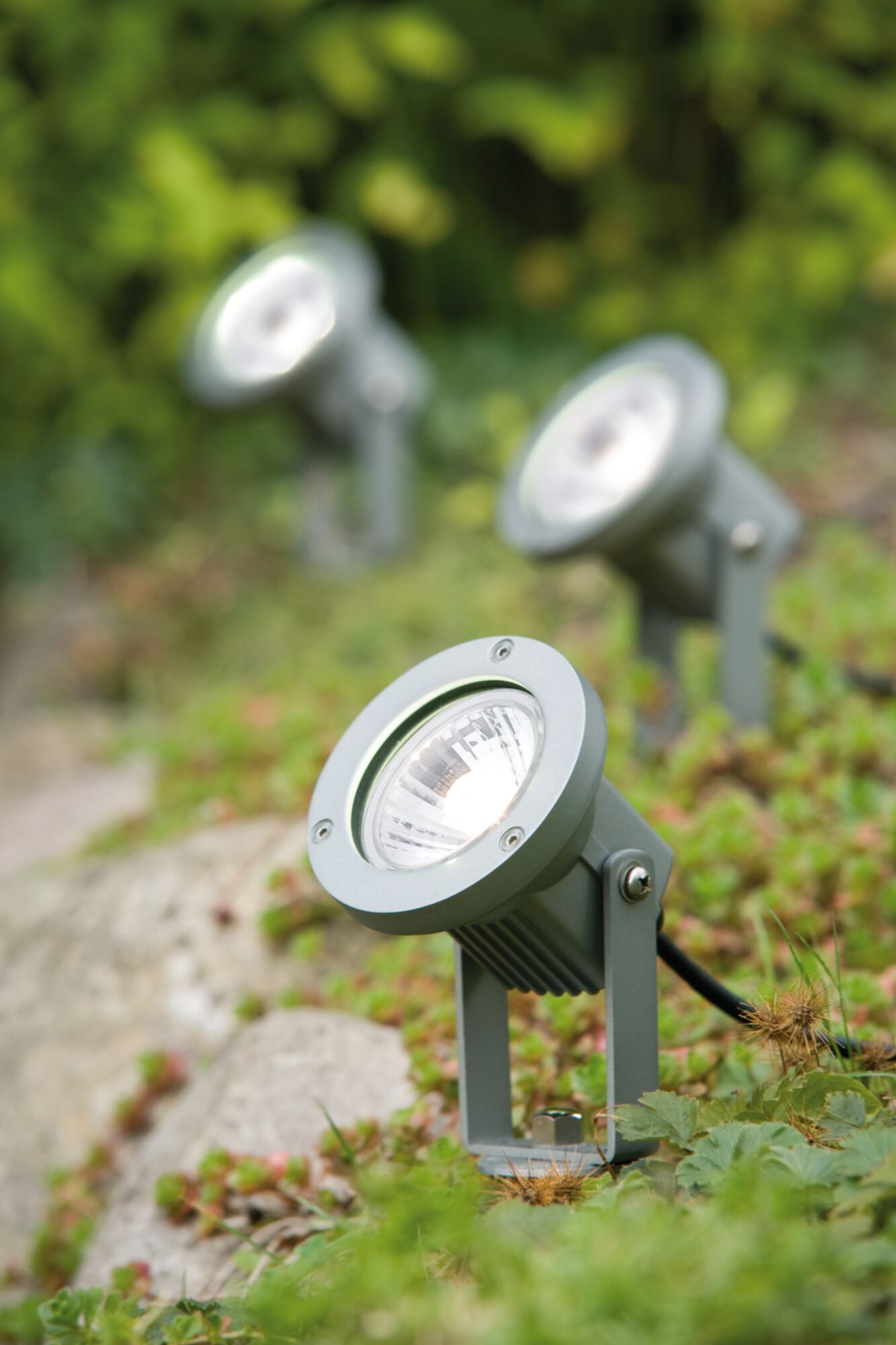Grauer Aluminium-Gartenstrahler mit LED-Licht auf grünem Boden für Außenbeleuchtung und Gartendekor.