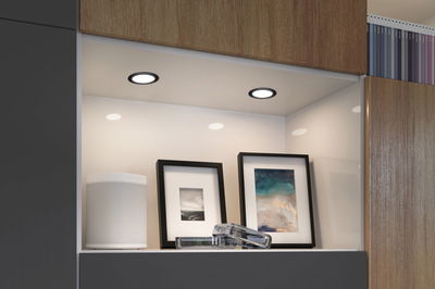 Two round LED recessed lights with black frames illuminate white shelf with speaker and picture frames.