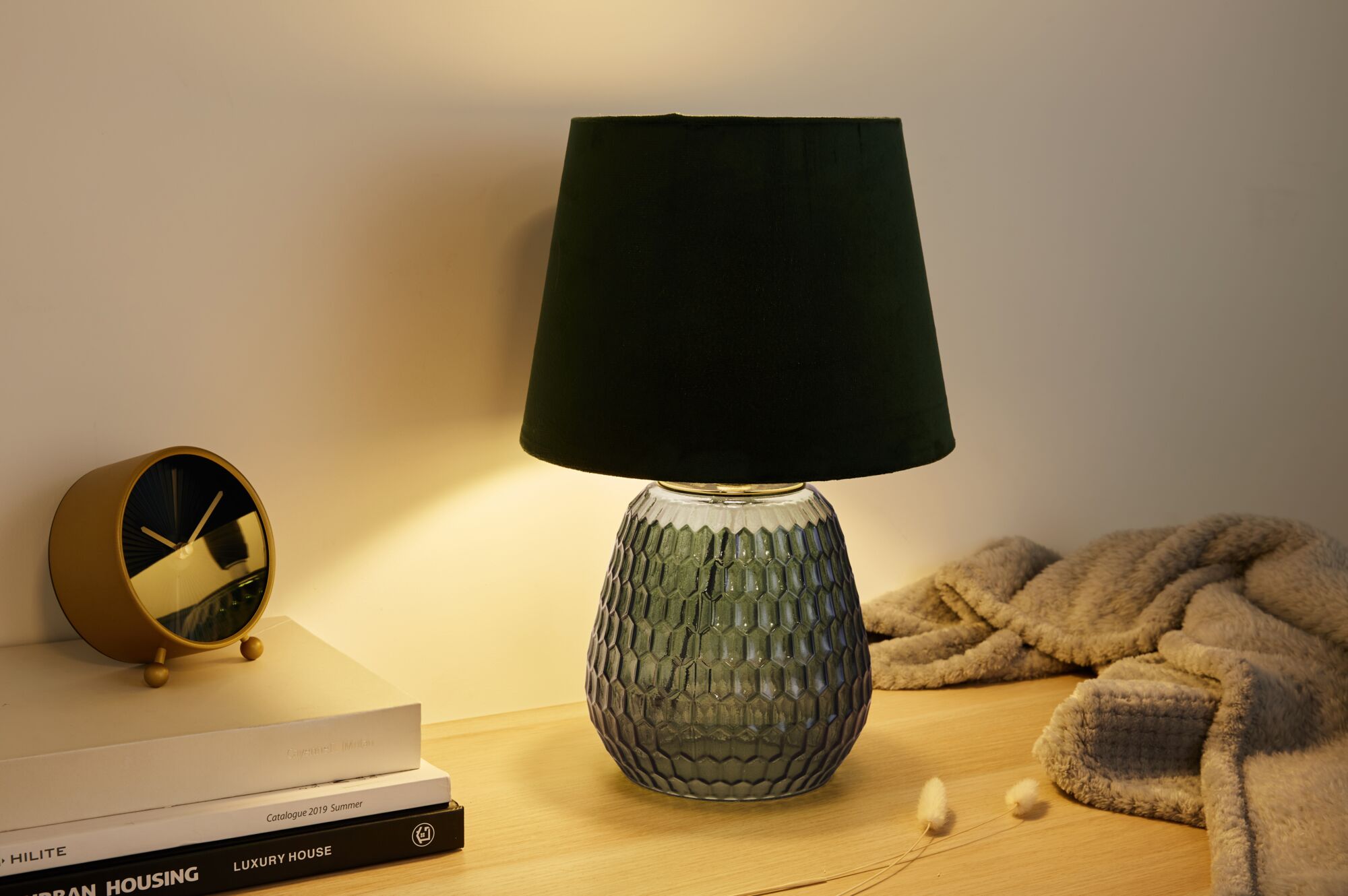 Groene glazen tafellamp met zwarte stoffen kap op houten oppervlak naast gouden klok en boeken