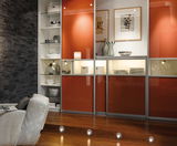 Salon moderne avec portes coulissantes orange laqué et éclairage LED indirect dans les étagères.