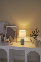 Lichtblauwe keramische tafellamp met witte stoffen kap op wit dressoir met decoratie en planten