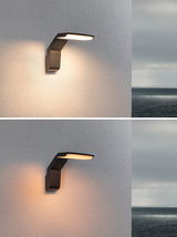 Moderne schwarze Außenwandleuchte aus Metall mit warmweißem LED-Licht an Hauswand mit Meerblick