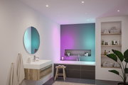 Modern bathroom with wooden vanity, round mirror, and bathtub featuring colorful LED lighting