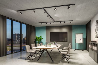 Moderne vergaderruimte met zwarte spots aan rails aan het plafond en grijze stoelen rond witte tafel