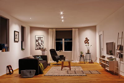 Modern living room with wooden floor, black sofa, armchair, and warm white LED ceiling lights.