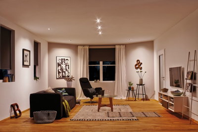 Salon moderne avec sol en bois, canapé noir, fauteuil et éclairage LED blanc chaud au plafond.