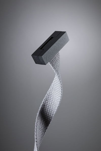 Black plastic part with twisted grey textile strap on grey background, lighting component detail