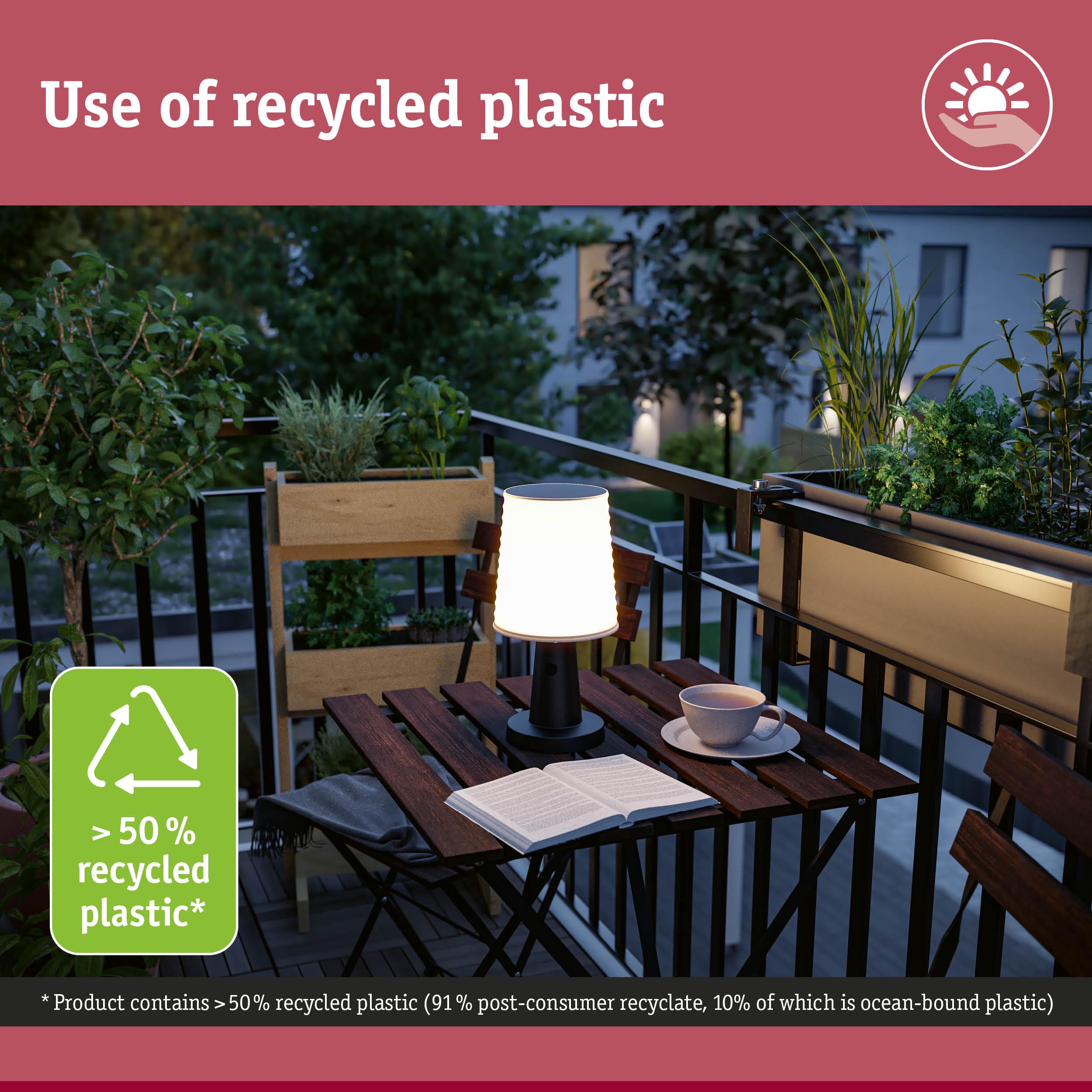 Illuminated table lamp made from recycled plastic on balcony with plants and book at dusk