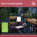 Illuminated table lamp made from recycled plastic on balcony with plants and book at dusk