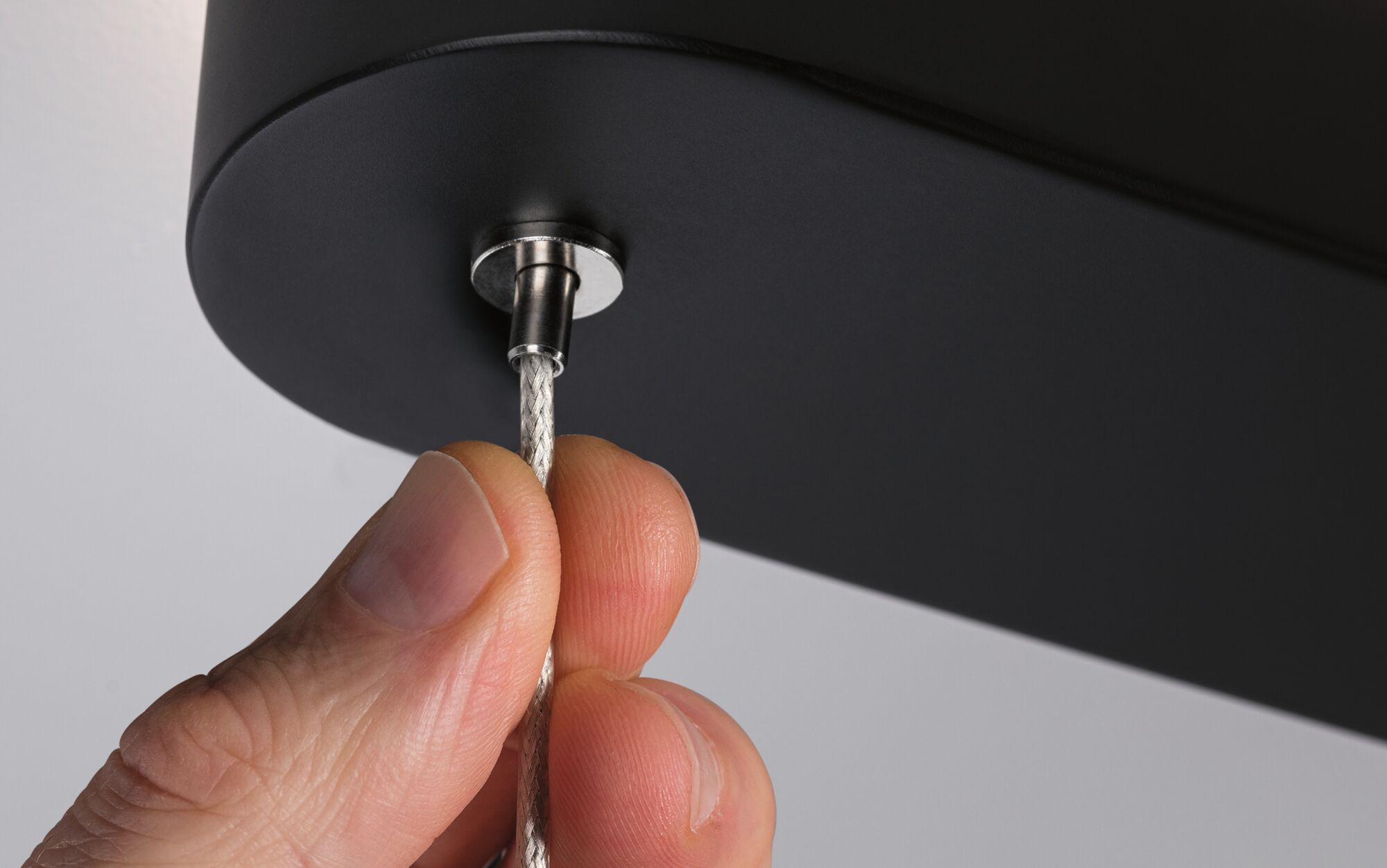 Hand holding silver steel cable attached to black metal lamp housing for modern lighting
