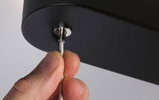 Hand hält silbernes Stahlseil an schwarzem Lampengehäuse aus Metall für moderne Beleuchtung