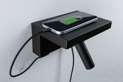 Schwarzes Wandregal aus Metall mit integriertem USB-Ladeanschluss und Smartphone mit grünem Akku-Symbol.