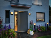 Moderne buitenverlichting met warm wit licht bij grijze voordeur en tuinpad met planten