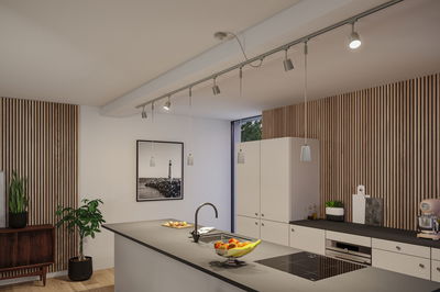 Moderne keuken met witte kasten, houten panelen, grijs werkblad en LED-railverlichting.