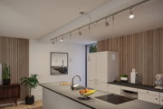 Moderne Küche mit weißen Schränken, Holzpaneelen und grauer Arbeitsplatte mit LED-Schienenbeleuchtung.