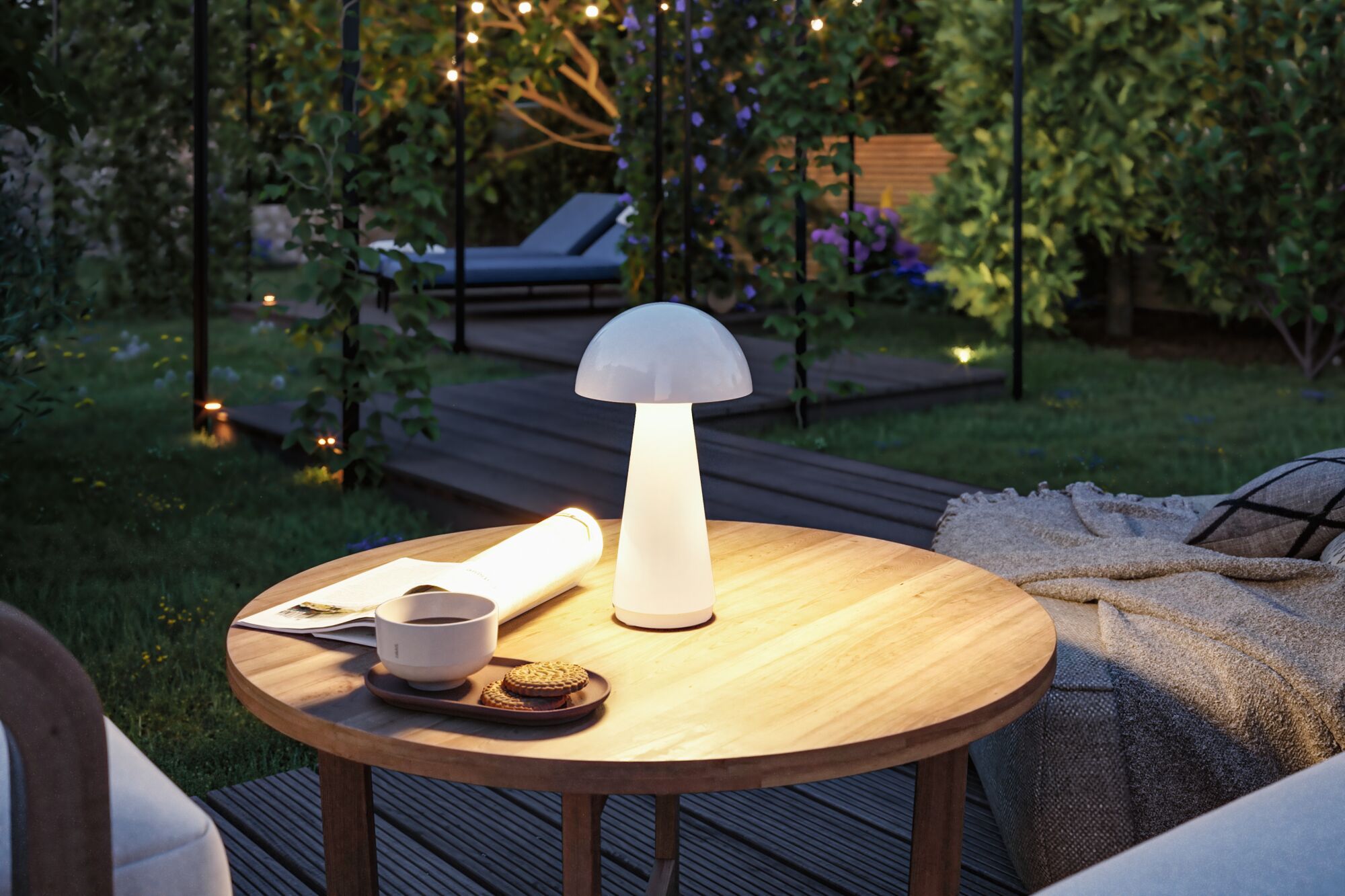 Weiße Pilzlampe aus Kunststoff auf Holztisch im Garten mit Tasse, Keksen und Decke für Outdoor-Beleuchtung