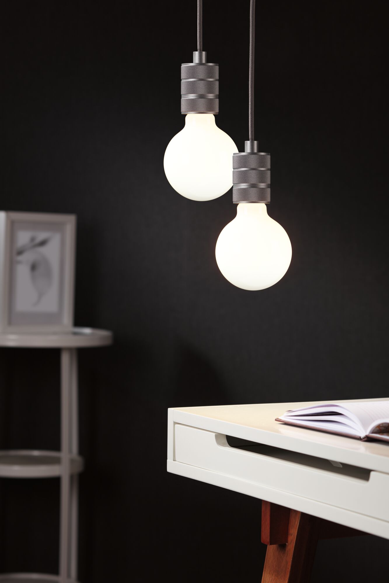 Zwei hängende LED-Glühbirnen mit grauen Metallfassungen vor schwarzem Hintergrund im modernen Arbeitszimmer