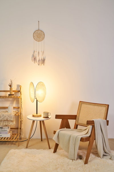 Cozy wooden chair with woven backrest and cream blanket beside modern table lamp in warm living room