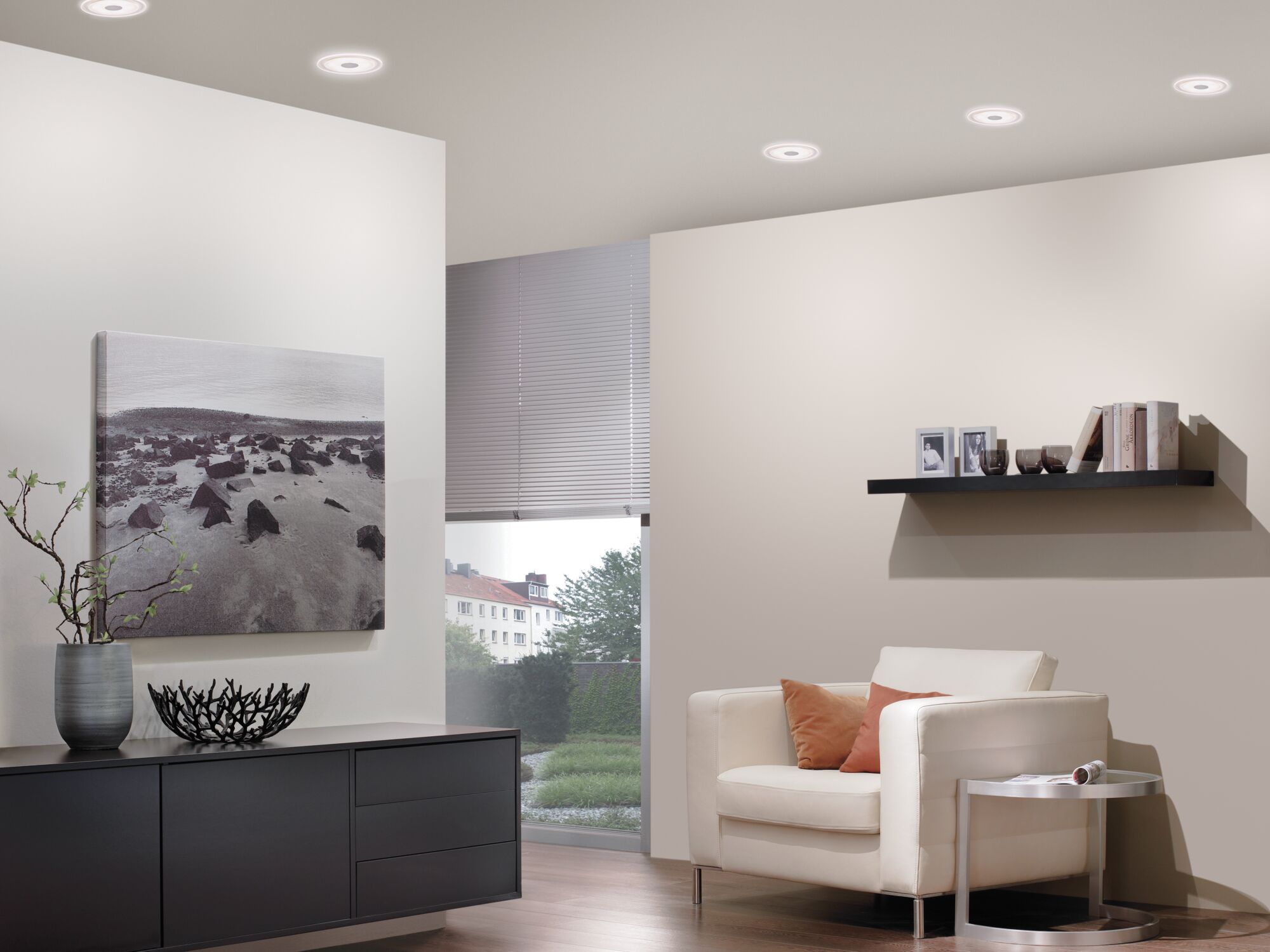 Salon moderne avec plafonniers LED blancs, fauteuil crème et buffet noir en bois sous lumière naturelle.