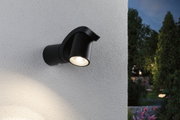 Schwarze Aluminium-Außenwandleuchte mit warmweißem LED-Strahler an weißer Wand im Garten.