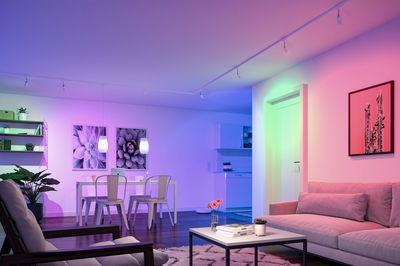 Modernes Wohnzimmer mit farbiger LED-Beleuchtung, Sofa und Esstisch in offener Raumgestaltung