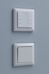 Twee witte kunststof wandschakelaars op blauwe muur, boven met LED-indicator, onder klassiek.