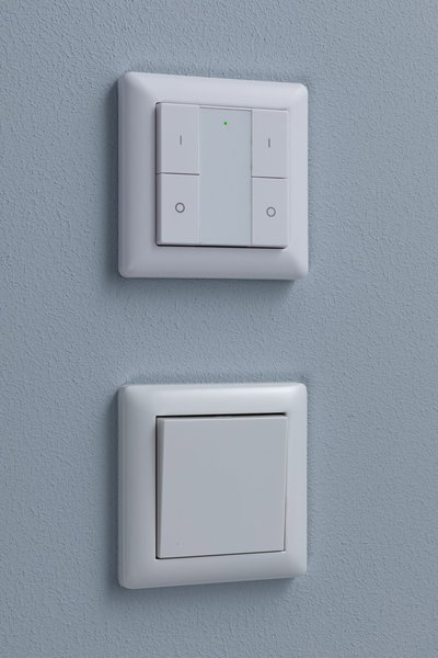 Two white plastic wall switches on blue wall, top with LED indicator, bottom classic design.