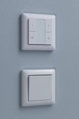 Twee witte kunststof wandschakelaars op blauwe muur, boven met LED-indicator, onder klassiek.