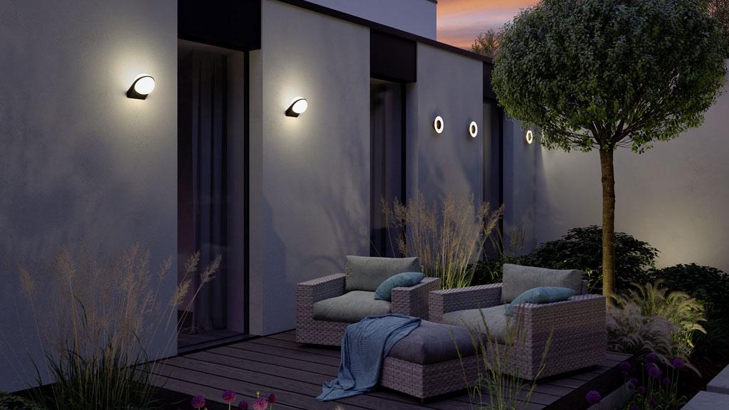 Moderne witte buitenwandlampen verlichten gezellige terras met rotanmeubilair bij schemering.