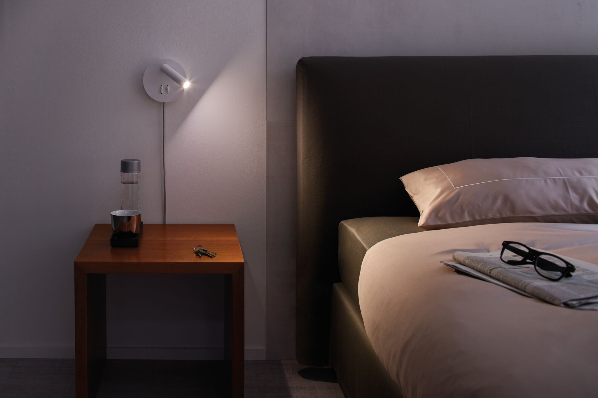 Moderner weißer LED-Wandleuchter mit schwenkbarem Spot über Nachttisch aus Holz im Schlafzimmer.